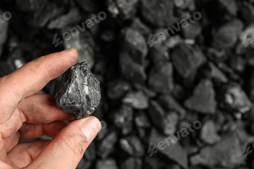 Preview: Man holding piece of coal over pile, closeup. Space for text