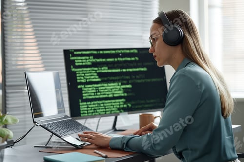 Preview: Young Adult Woman Writing Code on Laptop While Wearing Headphones