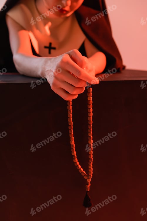 Preview: partial view of nun holding rosary isolated on pink, blurred background
