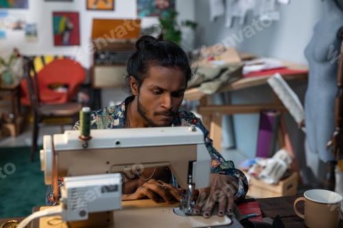 Preview: Young creative fashion designer bending over electric sewing machine