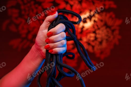 Preview: A delicate hand with a sexy red manicure holds a Shibari rope emphasizing the beauty of bondage art