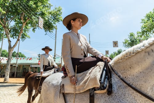 Preview: Young woman in hat sitting on horseback with both legs on side of saddle in daylight
