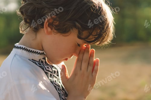 Preview: A young child wearing a traditional embroidered shirt quietly prays outdoors