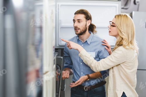 Preview: woman talking with consultant and pointing with finger at fridge in home appliance store
