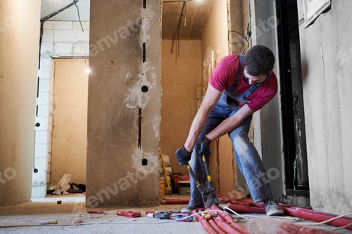 Preview: Male worker cutting pipe with cutter in empty apartment.