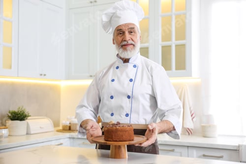 Preview: Elderly pastry chef at table with tasty cake in kitchen