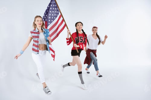 Preview: happy young multiethnic women walking with american flag and celebrating 4th july