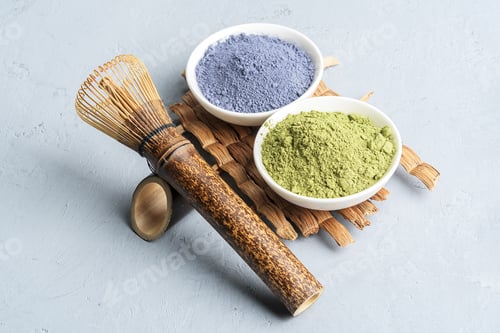 Preview: Bowls of different matcha tea powder and whisk on a concrete surface.