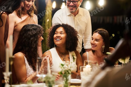 Preview: Happy young African American bride sitting by served table among friends
