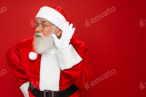 Preview: Santa Claus try hear you overhear listening intently isolated on plain red background studio.