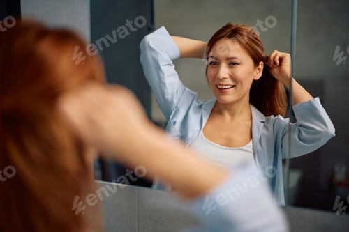Preview: Smiling Woman Adjusting Hair in Bathroom Mirror