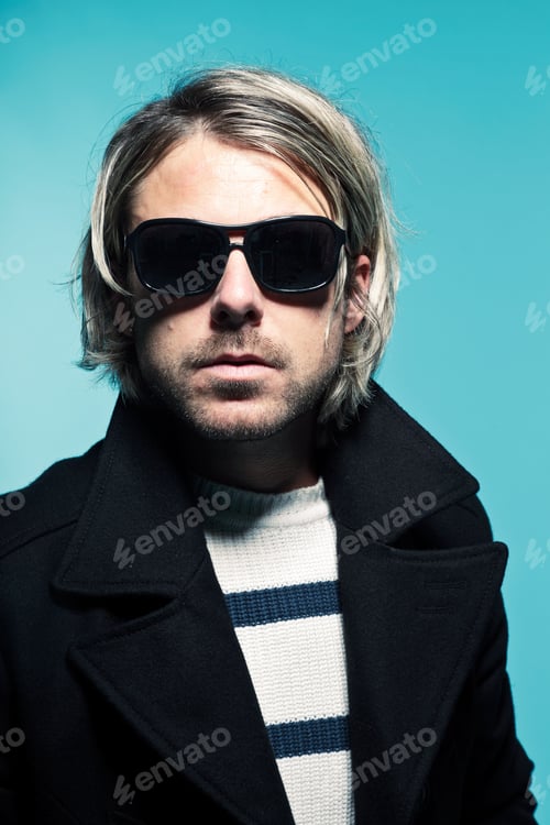 Preview: Studio Portrait Of Young Casual Man With Long Blond Hair Wearing Sunglasses And Black Jacket. Blue