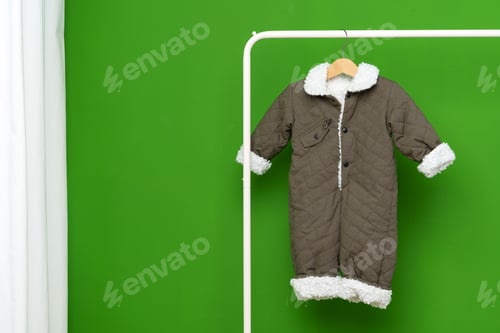 Preview: Kids winter coat hanging on hanger against green wall in studio