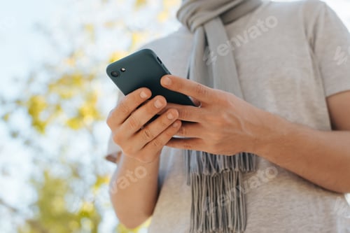 Preview: Close-up of male caucasian hands holding phone, unrecognizable man in scarf