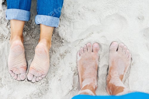 Preview: Sandy female and male feet on the beach in summer, top view