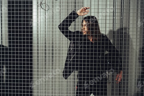 Preview: Stylish young long haired man in leather jacket holding helmet and looking through grid
