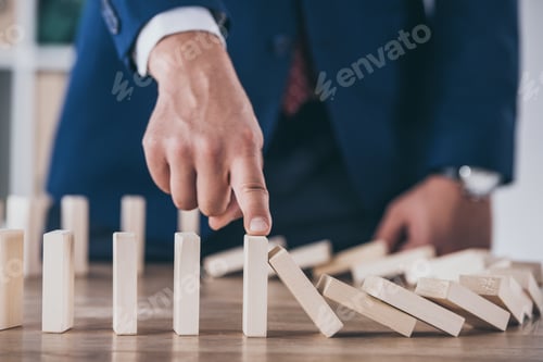 Preview: partial view of risk manager blocking domino effect of falling wooden blocks