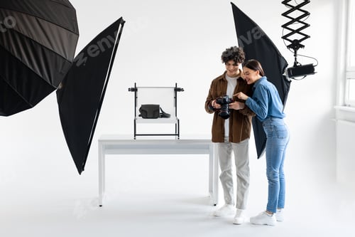 Preview: Team of professional photographer and female assistant checking the pictures on photocamera during