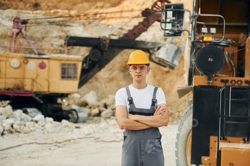 Preview: Standing in the front of vehicle. Worker in professional uniform is on the borrow pit at daytime