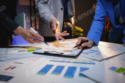 Preview: Business team working late, analyzing financial documents and pointing at charts on a desk