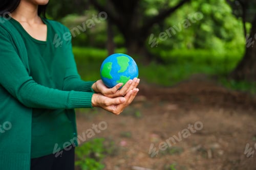 Preview: An Asian woman holds a globe in green forest,symbolizing importance preserving nature.emphasizes