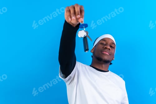 Preview: Black ethnic man in white clothes on a blue background happy with the new house keys