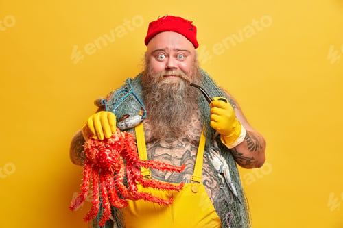 Preview: Photo of plump bearded seafarer caught big red octopus carries fishing net dressed in overalls has t