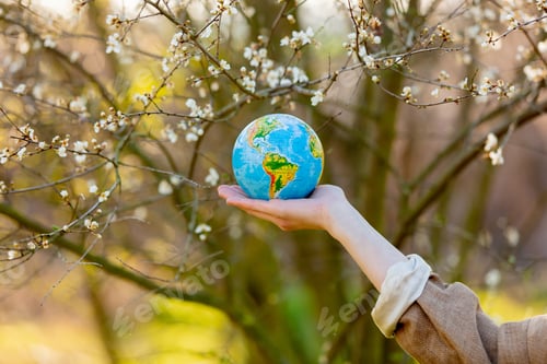 Preview: woman hand holds Earth globe in blooming cherry garden