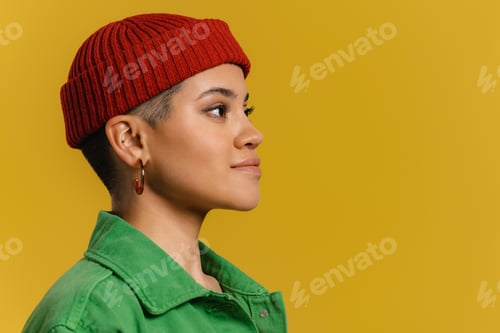 Preview: Side view of fashionable young woman in hat standing against yellow background