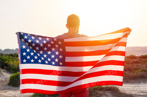Preview: Rear vew of man holding USA American flag against sunset sky outdoor. Independence day of USA