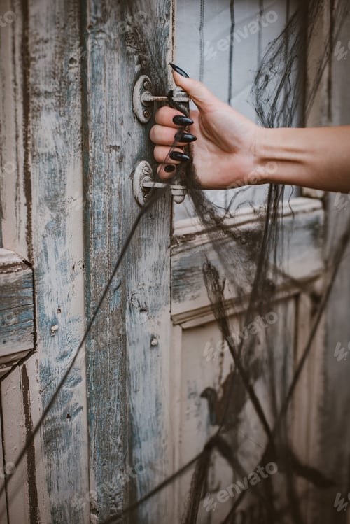 Preview: Halloween horror concept background. witch hand with black nails opens old wooden door spider web.