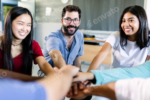Preview: Young multiethnic group of students stacking hands with male teacher in classroom