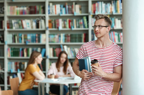 Preview: Young man with books and drink in library. Space for text