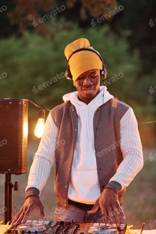 Preview: Young African man in casualwear and headphones mixing sounds on turntables