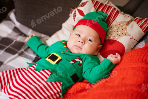 Preview: Beautiful half-year-old child lies on pillows and smiles in a red-green costume