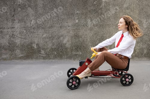 Preview: Funny businesswoman driving retro pedal car outdoor