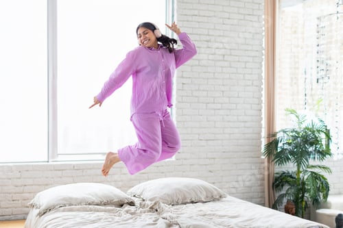 Preview: Joyful woman jumping on bed in pajamas