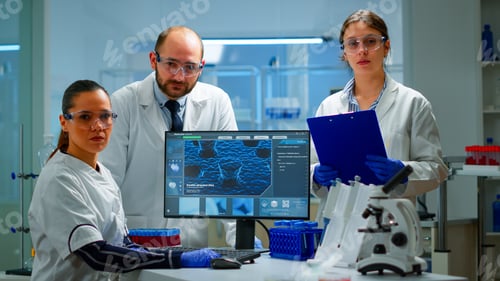 Preview: Team of scientists sitting in laboratory looking at camera
