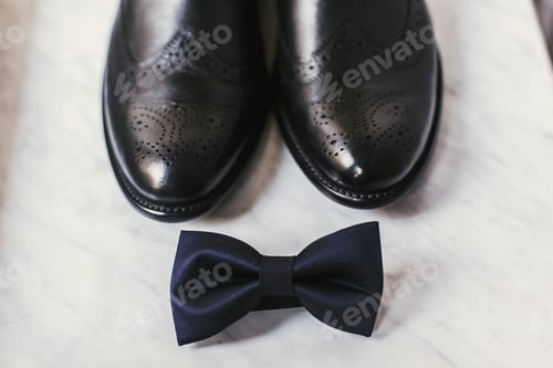 Preview: Stylish black shoes and navy bow tie on marble background