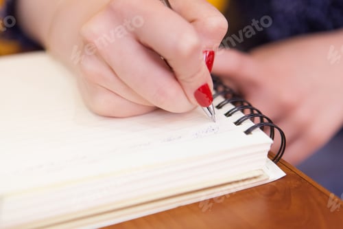 Preview: Closeup shot of a female's handholding a pen and writing something in a textbook