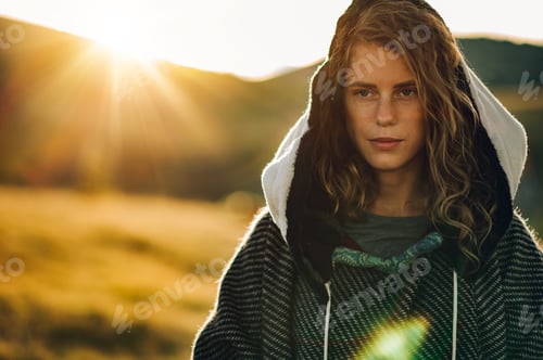 Preview: Portrait of a stylish woman hiking on a mountain path with tall grass.