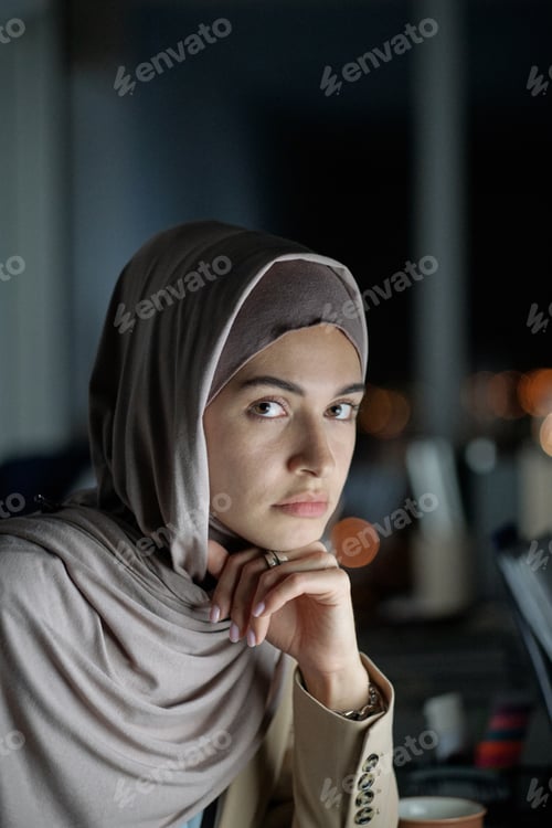 Preview: Young confident businesswoman in hijab sitting by workplace