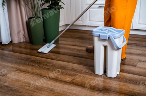 Preview: Housewife cleans floor with flat mop. Woman in orange pants washes wooden laminate