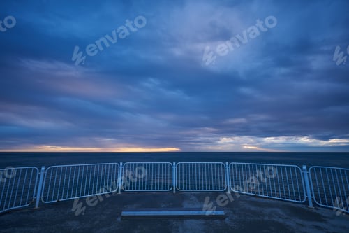 Preview: deserted pier with dramatic sky over stormy dark sea at sunrise