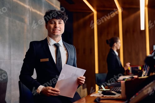 Preview: Happy concierge at hotel reception desk looking at camera.