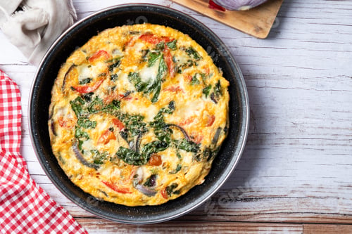 Preview: Italian Frittata made with spinach, tomatoes, onion and peppers on white wooden table