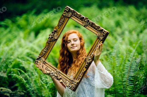 Preview: Young woman holding gold picture frame amongst forest ferns