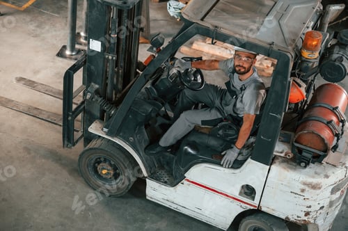 Preview: View from the top, in the forklift. Young factory worker in grey uniform