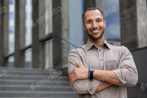 Preview: Portrait of a smiling young Muslim businessman in a shirt standing near an office building, smiling