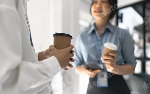 Preview: Couple of happy colleagues talking while standing at the office window with cups of coffee